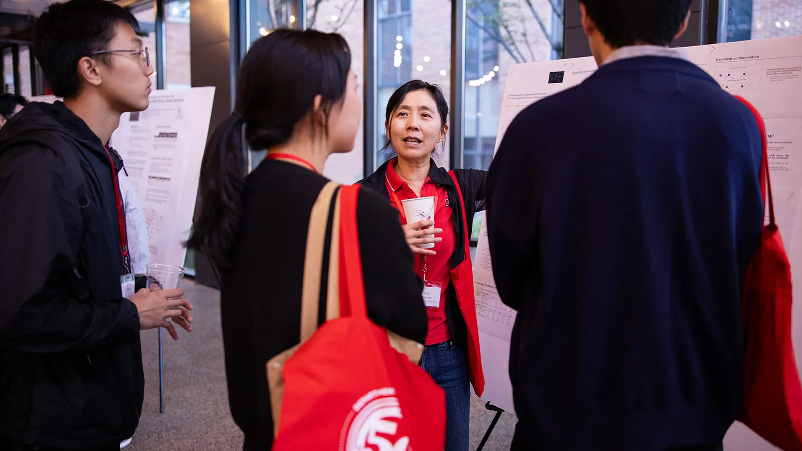 an alumna presenting research to three graduate students standing in front of a poster