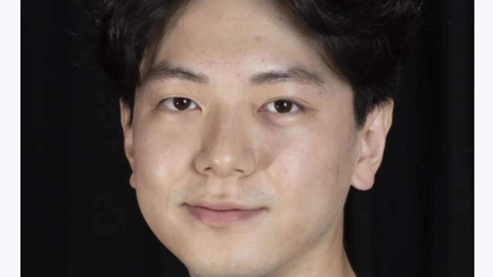 Jae Ho in a gray shirt in front of a black back drop