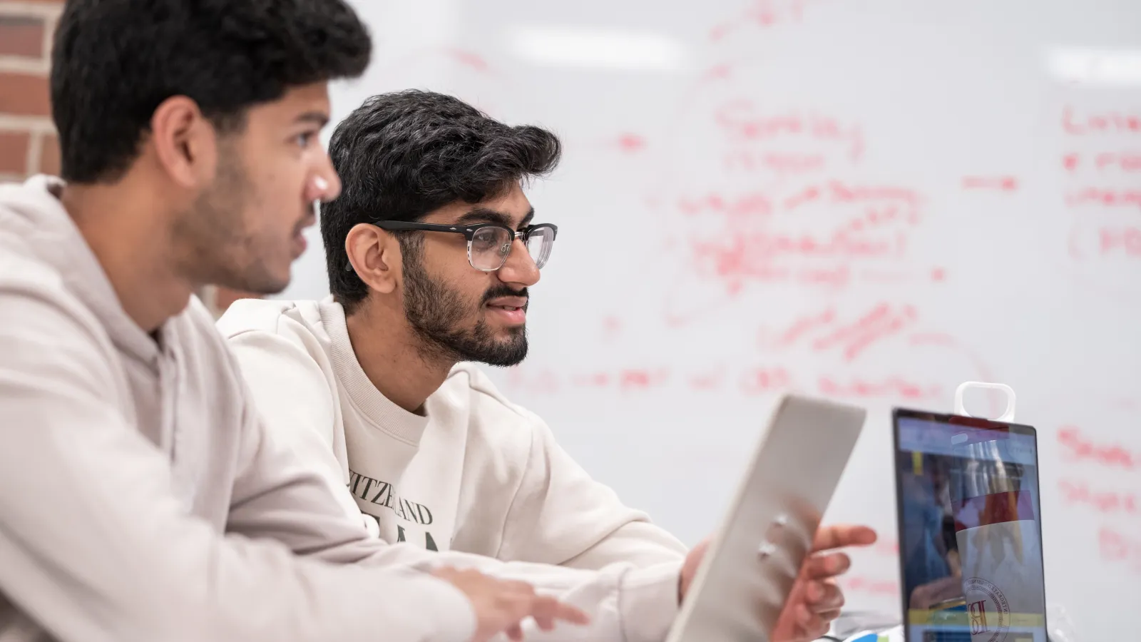three students sitting at a table discussing statistics in front of a white board