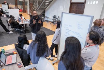 An instructor speaking with four students in front of a white board