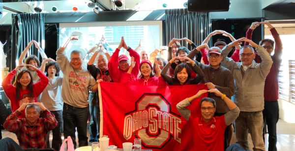 Ohio State fans and alumni posing together with a flag