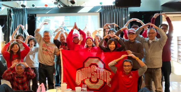 Ohio State fans and alumni posing together with a flag