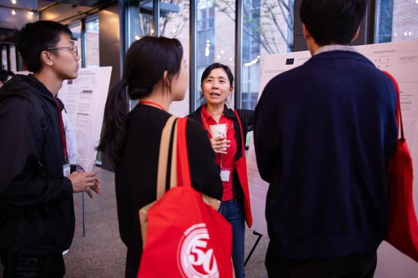 an alumna presenting research to three graduate students standing in front of a poster