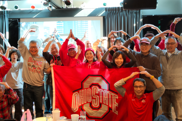 Ohio State fans and alumni posing together with a flag