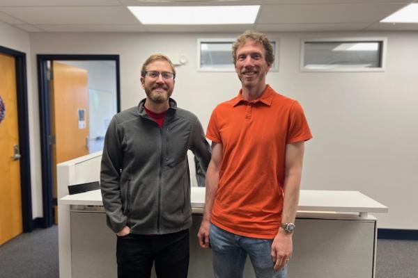 Tom and David standing together and smiling in front of a desk