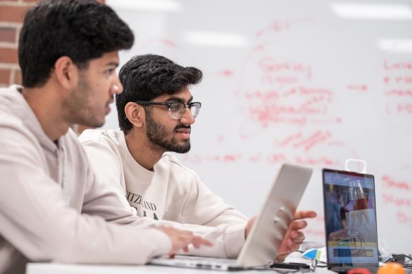 three students sitting at a table discussing statistics in front of a white board