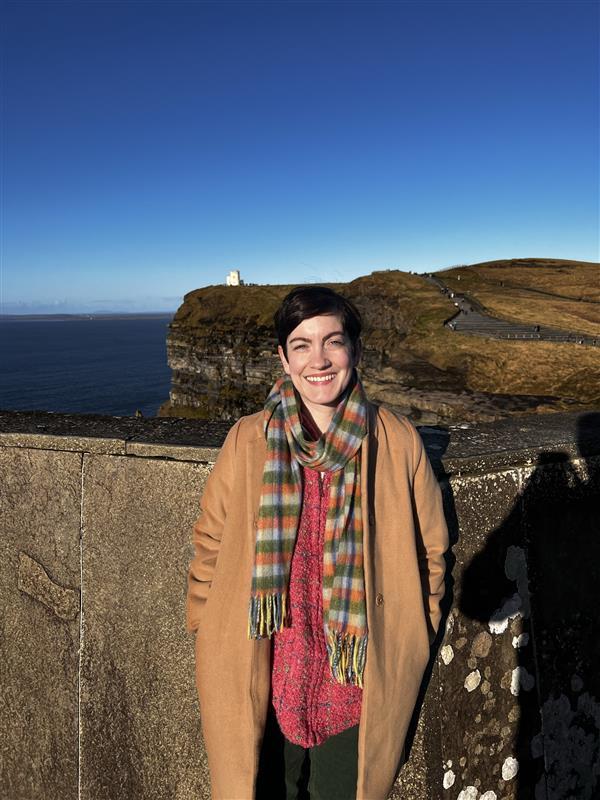 Cassie wearing a coat and standing in front of a seaside cliff.