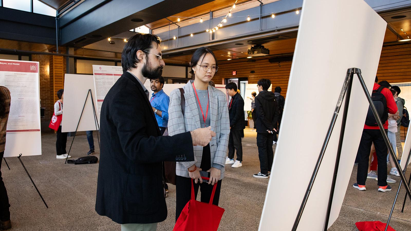 presenter and observer standing in front of a poster discussing research