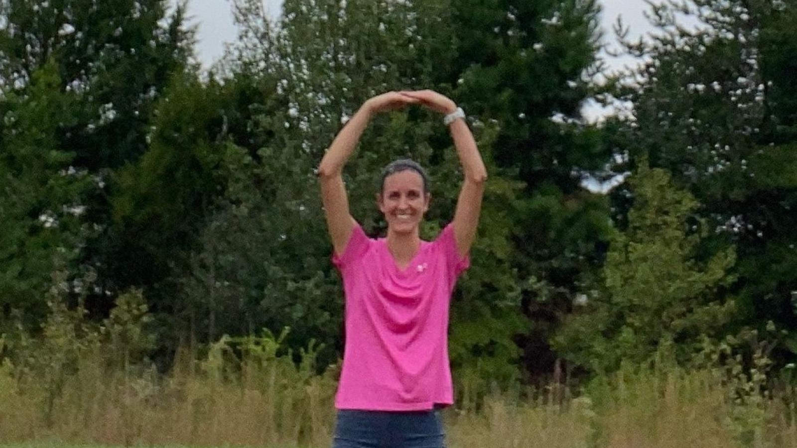 Staci Hepler standing in front of trees making an O with her arms