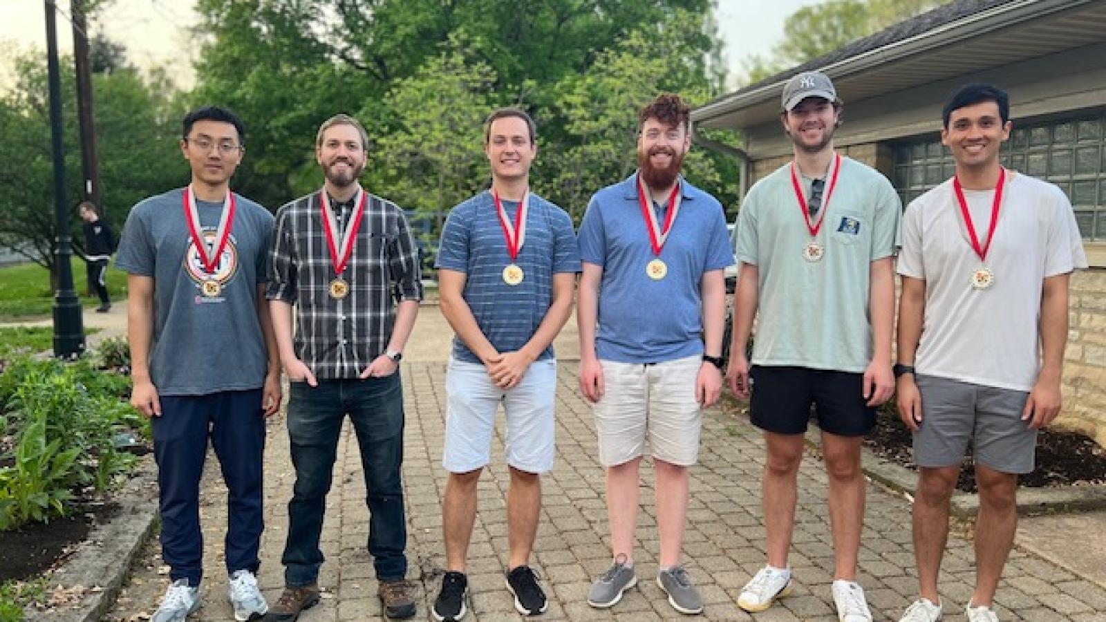Cornhole winners standing in a row and wearing medals
