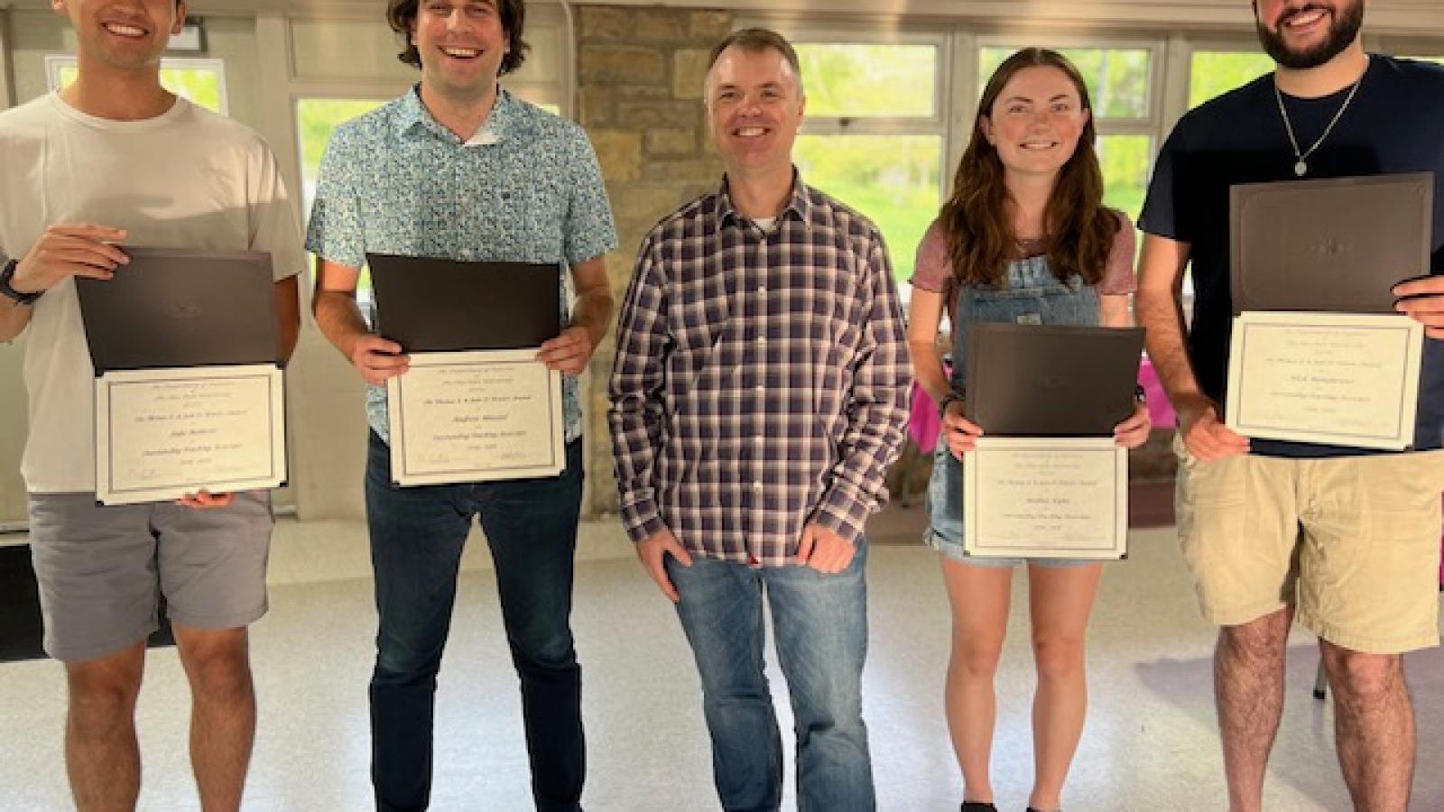 Powers TA Award Recipients Jacob Roberts, Andrew Heeszel, Andrea Kuhn, and Nicholas Mandarano standing with Christopher Hans and holding certificates