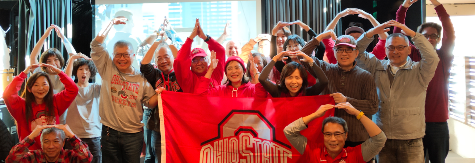 Ohio State fans and alumni posing together with a flag